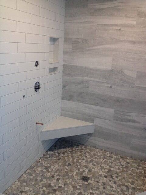Walk-in shower with wood-look plank tile, white subway walls, a recessed niche, corner bench and pebble mosaic floor