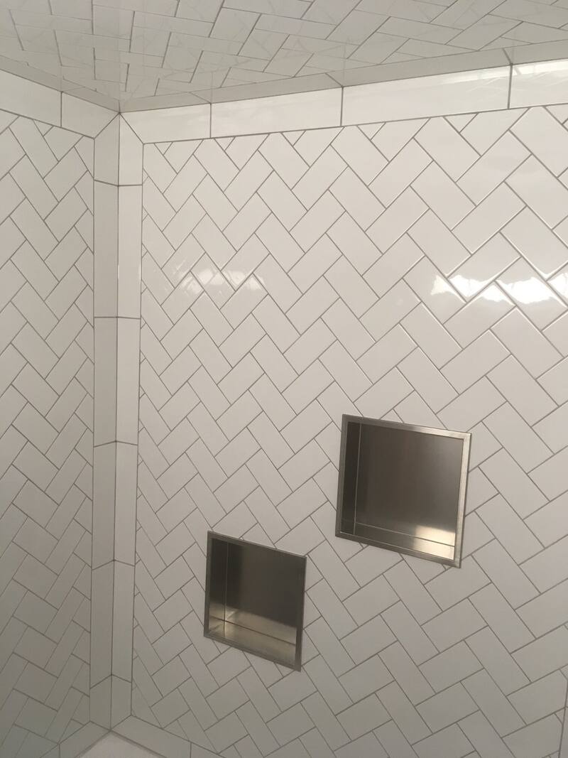 White herringbone tile on the shower walls and ceiling with two stainless steel recessed niches