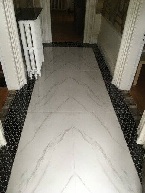 Large-format marble-look floor tile in a hallway, edged with a black hexagon mosaic border
