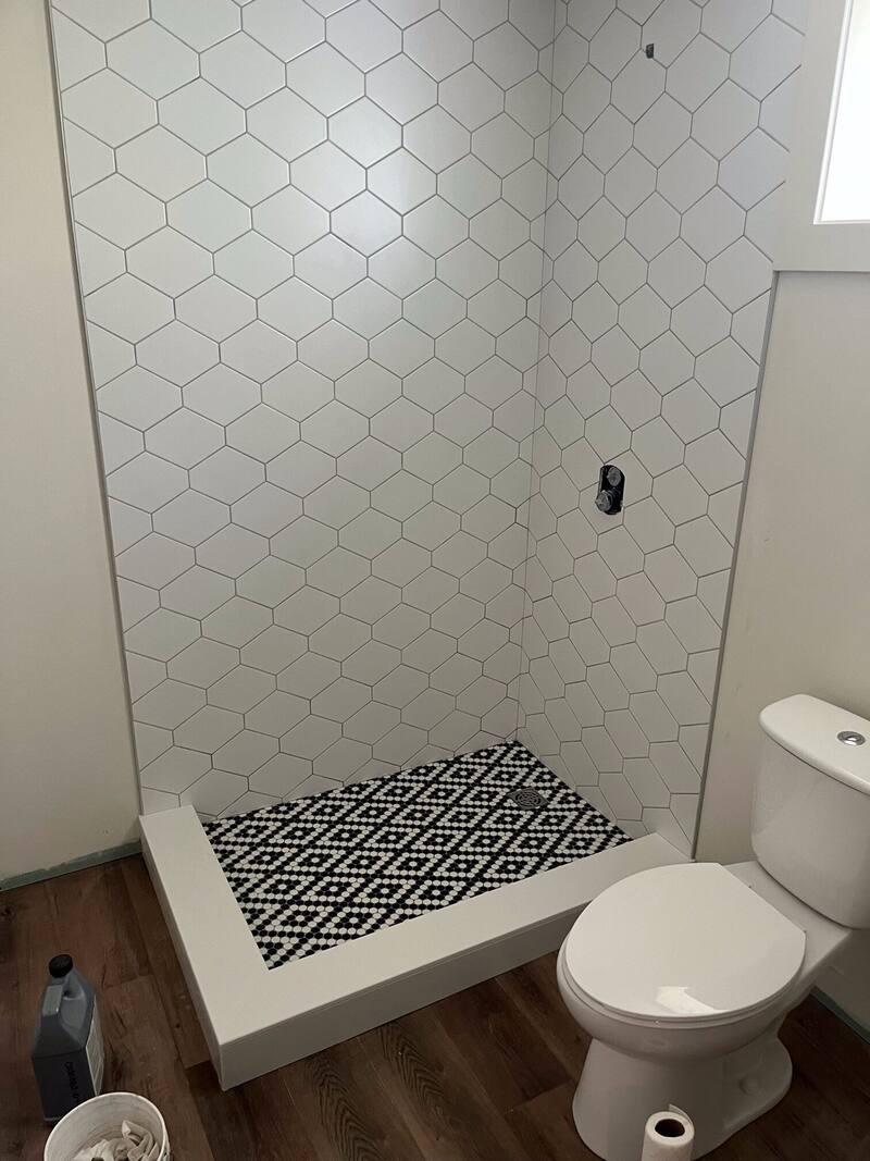 Shower with white hexagon wall tile and a black and white geometric mosaic shower floor