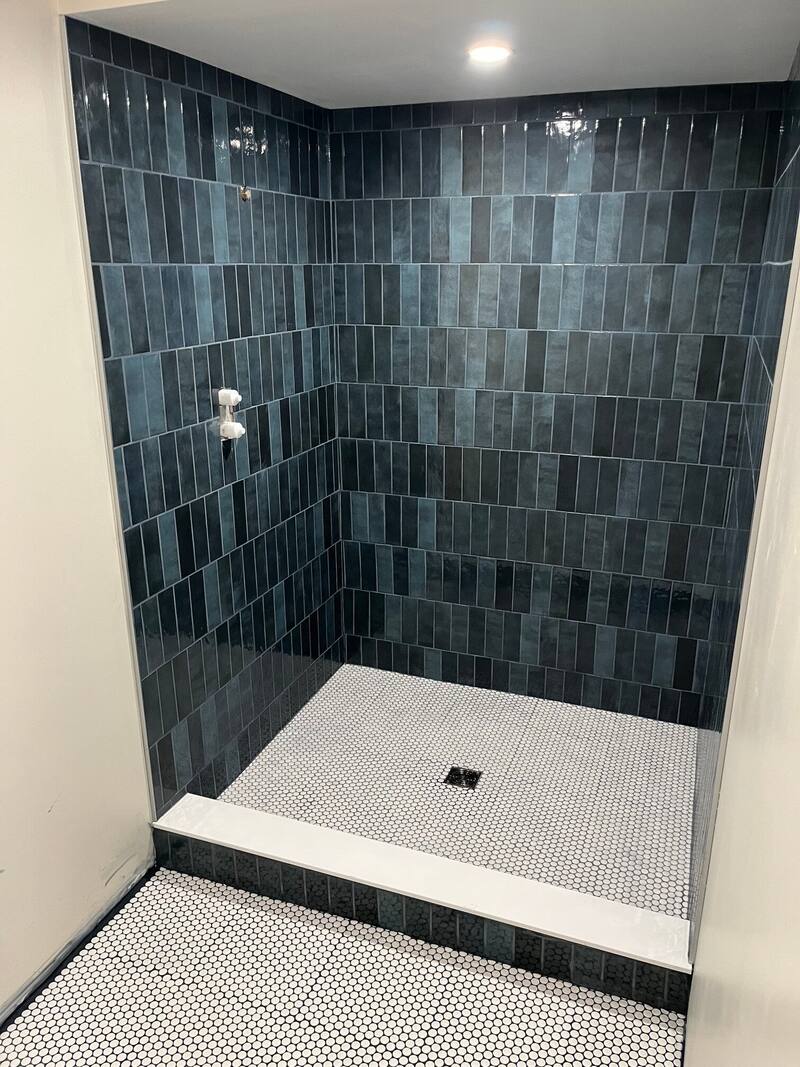 Walk-in shower with deep blue vertically stacked wall tile and a white penny round mosaic floor